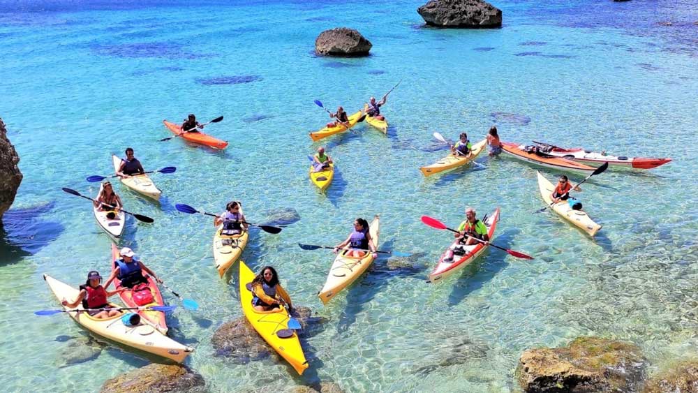 Gruppo di studenti in kayak nelle acque cristalline della Sardegna durante una gita scolastica outdoor