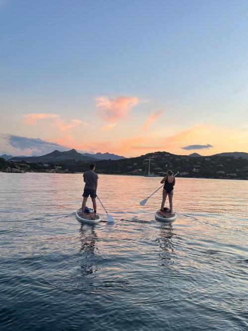 Freunde auf einem SUP-Ausflug bei Sonnenuntergang im Meer an der Costa Smeralda