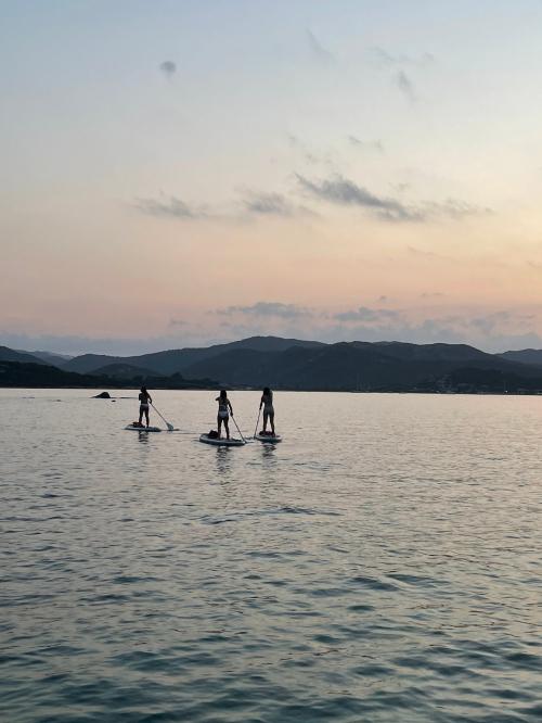 Freunde auf einem SUP-Ausflug bei Sonnenuntergang im Meer an der Costa Smeralda