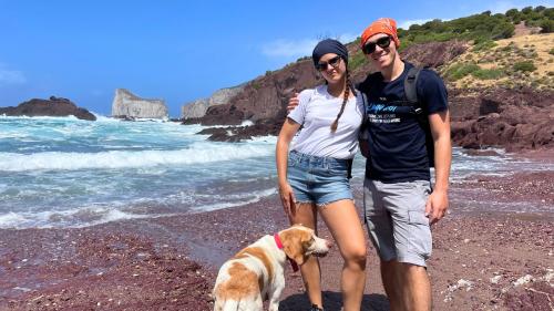 coppia con cane sulla costa di Nebida con lo scoglio di Pan di Zucchero sullo sfondo