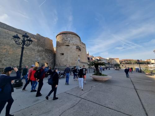 Cinta muraria con torre troneggia sul porto di Alghero con turisti 