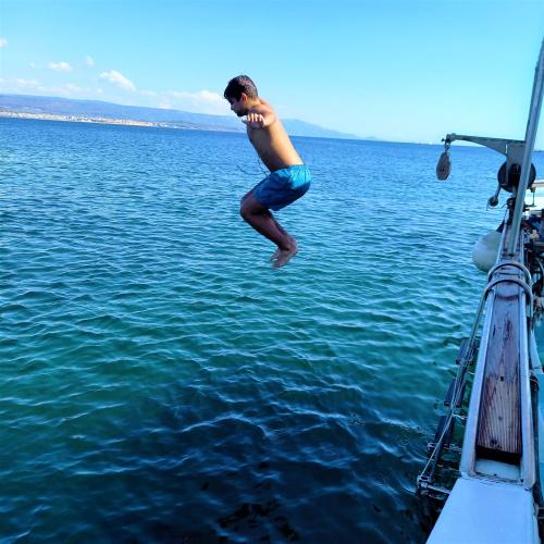 Bambino tuffa da una barca nel mare turchese della zona di Alghero