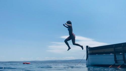 Una ragazza si tuffa dalla barca a vela d'epoca nell'acqua azzurra di Alghero