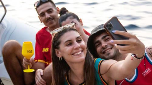 Young boys take a photo during a dinghy excursion at sunset in Porto Flavia with aperitifs