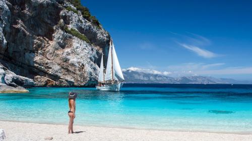 Girl watches from the beach the vintage sailing ship in the blue water of the Gulf of Orosei