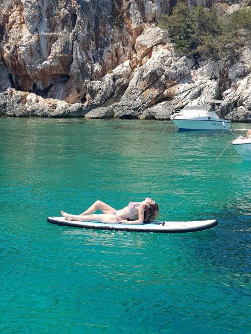 Girl lying in SUP during boat excursion in the Gulf of Alghero
