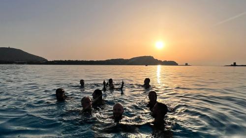 Persone felici fanno il bagno al tramonto a La Pelosa