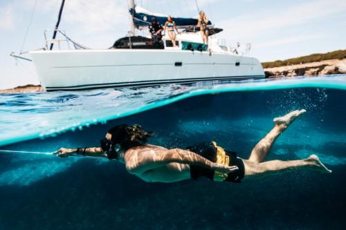 Garçon nage dans l'archipel de La Maddalena avec catamaran en arrière-plan